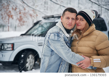 Beautiful couple standing near the car in the winter forest Beautiful couple standing near the car in the winter forest 130179303