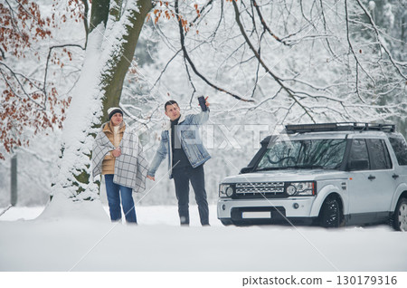 Walking and traveling. Beautiful couple standing near the car in the winter forest 130179316