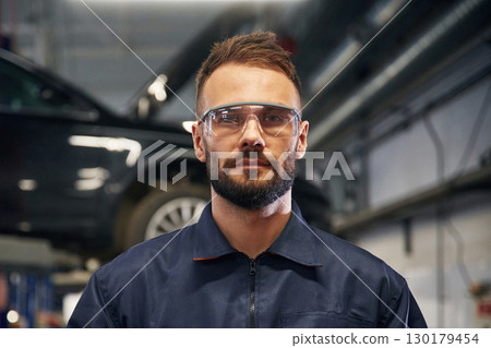 Looking at the camera. Car repairman is in the garage with automobile Looking at the camera. Car repairman is in the garage with automobile 130179454