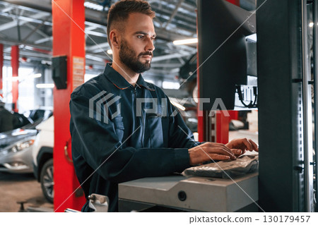 Working by computer. Car repairman is in the garage with automobile Working by computer. Car repairman is in the garage with automobile 130179457