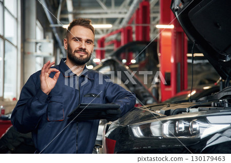 Using tablet. Car repairman is in the garage with automobile 130179463