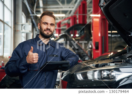 Using tablet. Car repairman is in the garage with automobile 130179464