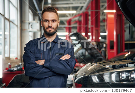With arms crossed, standing. Car repairman is in the garage with automobile 130179467