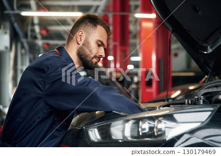 Busy car repairman is in the garage with automobile, fixing it 130179469