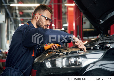 Professional electro device in hands. Car repairman is in the garage with automobile 130179477
