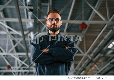 Standing and posing. Car repairman is in the garage with automobile 130179499