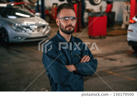 Standing and posing. Car repairman is in the garage with automobile 130179500