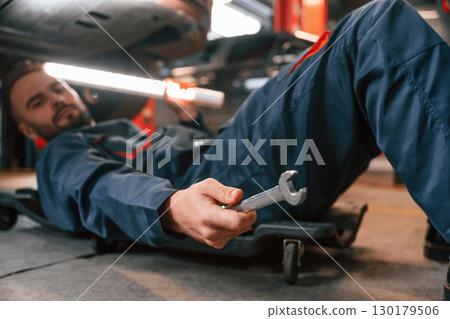Lying down on the ground. Car repairman is in the garage with automobile 130179506