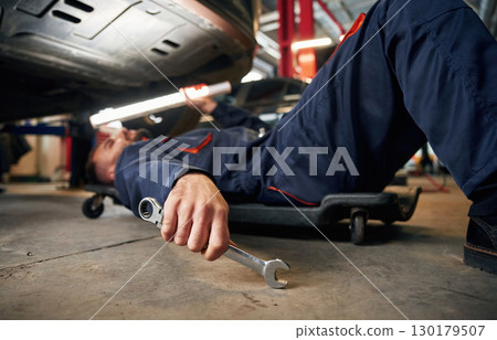 Lying down on the ground. Car repairman is in the garage with automobile 130179507