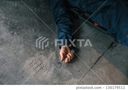 Repairman is lying down on the ground with tool in hand 130179511