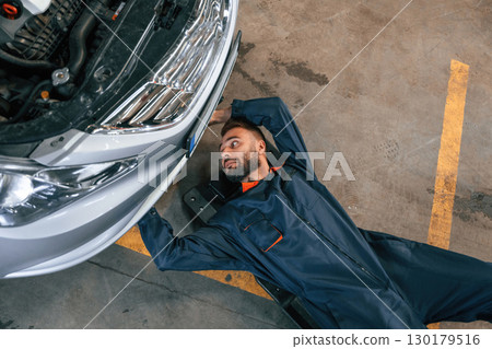On the ground with tool. Car repairman is in the garage with automobile On the ground with tool. Car repairman is in the garage with automobile 130179516