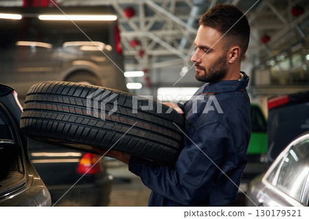 Holding a tire. Car repairman is in the garage with automobile Holding a tire. Car repairman is in the garage with automobile 130179521
