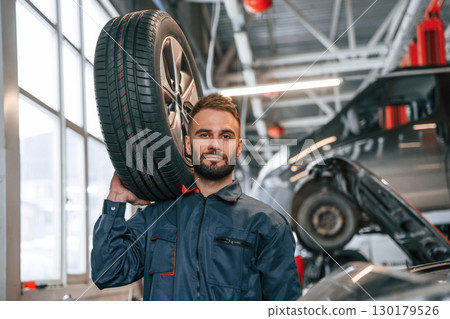 Holding a tire. Car repairman is in the garage with automobile Holding a tire. Car repairman is in the garage with automobile 130179526