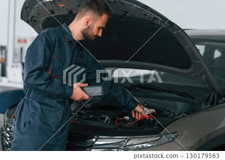 With device for measuring electricity. Car repairman is in the garage with automobile 130179563