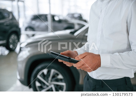 Black colored tablet in hands. Worker in formal clothes is in the auto salon 130179573