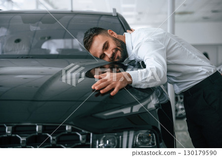 Embracing the car. Worker in formal clothes is in the auto salon Embracing the car. Worker in formal clothes is in the auto salon 130179590