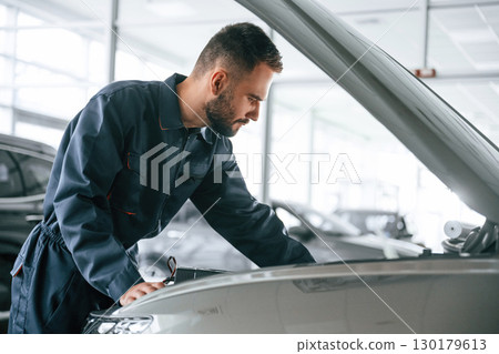Hood of vehicle is opened. Car repairman is in the garage with automobile 130179613