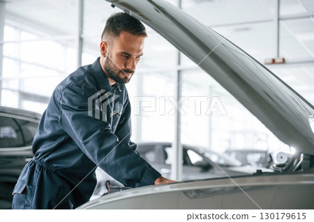 Side view, hood is opened. Car repairman is in the garage with automobile Side view, hood is opened. Car repairman is in the garage with automobile 130179615