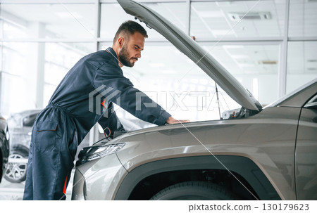 Fixing the vehicle. Side view. Car repairman is in the garage with automobile Fixing the vehicle. Side view. Car repairman is in the garage with automobile 130179623