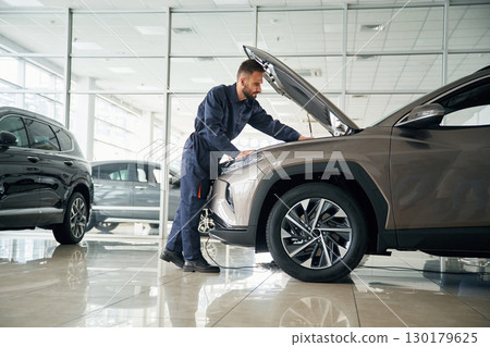 Focused on fixing the vehicle. Car repairman is in the garage with automobile 130179625