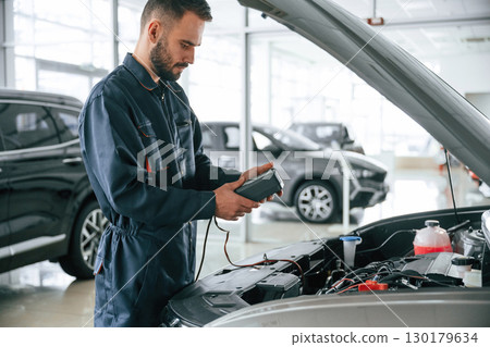Device for measuring voltage is in hands. Car repairman is in the garage with automobile 130179634