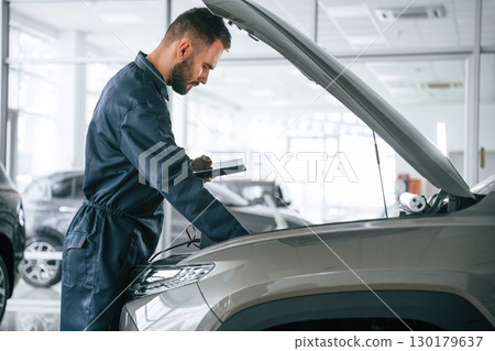 View from the side. Car repairman is in the garage with automobile View from the side. Car repairman is in the garage with automobile 130179637