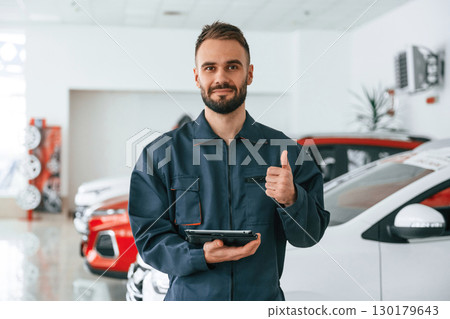 Standing and holding tablet in hands. Car repairman is in the garage with automobile Standing and holding tablet in hands. Car repairman is in the garage with automobile 130179643
