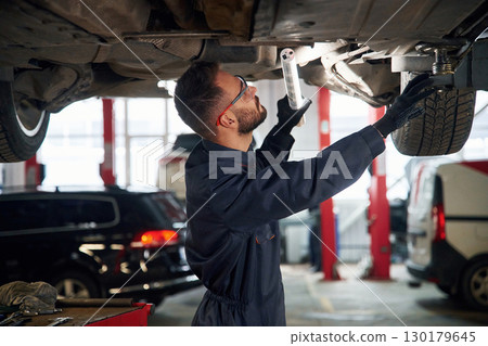 Under the vehicle, fixing. Car repairman is in the garage with automobile Under the vehicle, fixing. Car repairman is in the garage with automobile 130179645