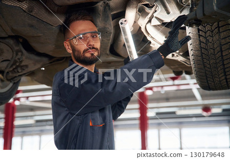 Under the vehicle, fixing. Car repairman is in the garage with automobile 130179648