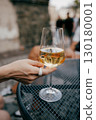 Woman with white ring holding glass of chilled white wine, sitting at metal table in an outdoor cafe, savoring tranquil moment under warm sunlight. Woman wearing white ring grasping white wine glass 130180001