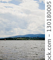 Sailboats are peacefully navigating lake on partly cloudy day, with mountains and small village visible in background, creating serene and picturesque scene. Sailboats gliding across calm lake waters 130180005