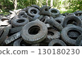 There is a large collection of discarded tires that have been haphazardly stacked in a natural wooded area 130180230