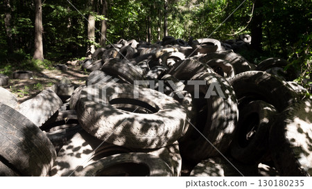 A large accumulation of discarded rubber tires piles up in a forest environment, exposing the critical ecological issues related to pollution and waste management. A large accumulation of discarded rubber tires piles up in a forest environment, exposing the critical ecological issues related to pollution and waste management. 130180235