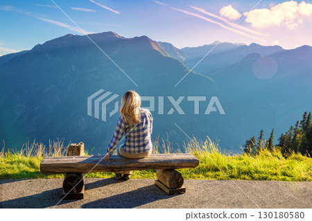 Mountain landscape on a sunny day. A woman sits on the bench and looks at the mountains. Grossglockner High Alpine Road. Austria, Europe Mountain landscape on a sunny day. A woman sits on the bench and looks at the mountains. Grossglockner High Alpine Road. Austria, Europe 130180580
