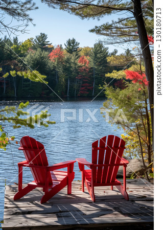 Two vibrant red adirondack chairs on a dock with scenic lake view 130180713