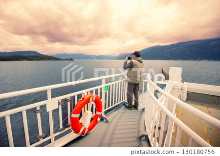 A man is sailing on a ferry. A man is standing on the deck and taking a photo from the ship 130180756
