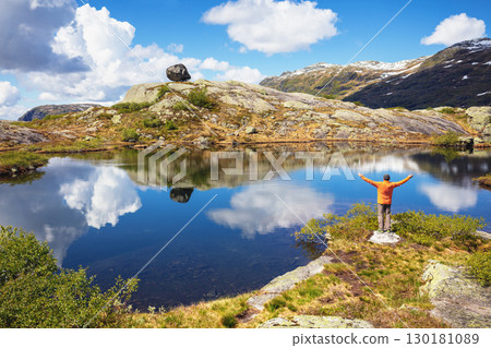Man with hands in the air standing on a lakeshore in the mountains. Nature park in Sauda municipality, Rogaland fylke. Beautiful nature of Norway, Europe Man with hands in the air standing on a lakeshore in the mountains. Nature park in Sauda municipality, Rogaland fylke. Beautiful nature of Norway, Europe 130181089