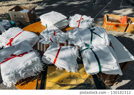 Bundles of white vintage linens tied with colorful ribbons displayed on a round table at a flea market. Sustainable living, secondhand textiles, local markets, decorative reuse 130181312
