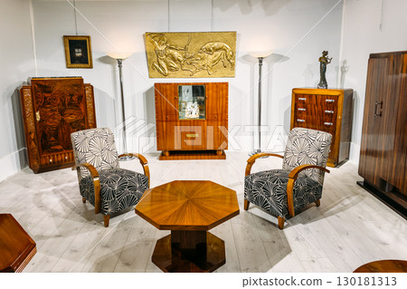 A vintage living room setup with patterned armchairs, polished wooden cabinets, and a gold wall relief. Art Deco design, vintage elegance, heritage revival, modern nostalgia 130181313