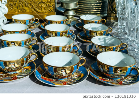 Close-up of ornate porcelain tea cups and saucers with gold details and hand-painted portraits. Thrifting elegance, flea market treasures, curated vintage finds, sustainable luxury Close-up of ornate porcelain tea cups and saucers with gold details and hand-painted portraits. Thrifting elegance, flea market treasures, curated vintage finds, sustainable luxury 130181330