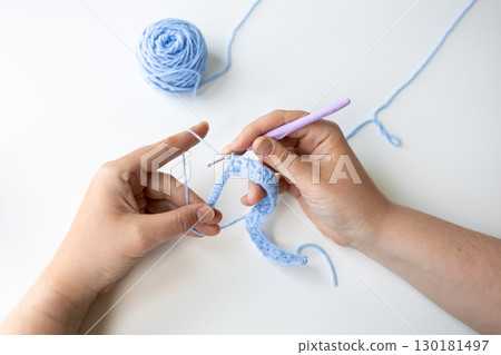 Close up of caucasian adult hand crocheting with blue yarn on white surface 130181497