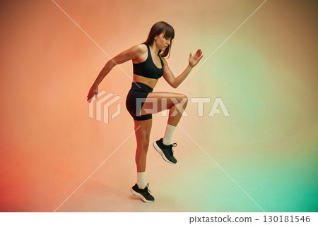 Standing on the one leg, side view. Young woman in fitness clothes is in the studio Standing on the one leg, side view. Young woman in fitness clothes is in the studio 130181546