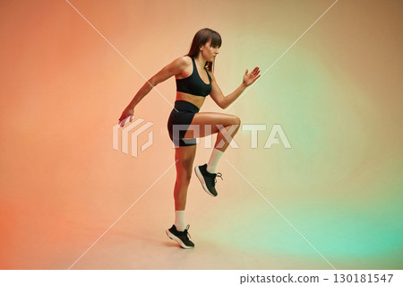 Standing on the one leg, side view. Young woman in fitness clothes is in the studio Standing on the one leg, side view. Young woman in fitness clothes is in the studio 130181547