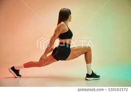 Side view, doing exercise. Young woman in fitness clothes is in the studio Side view, doing exercise. Young woman in fitness clothes is in the studio 130181572