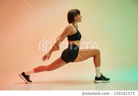 Side view, doing exercise. Young woman in fitness clothes is in the studio Side view, doing exercise. Young woman in fitness clothes is in the studio 130181573