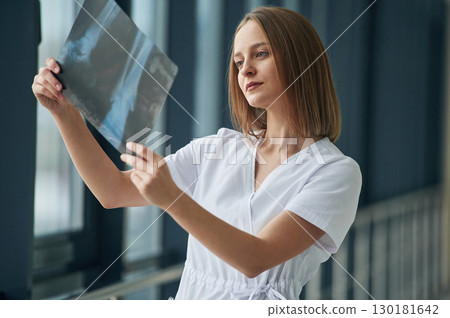 Examining x-ray. Female doctor in white coat is in the hall Examining x-ray. Female doctor in white coat is in the hall 130181642