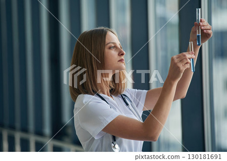 Mixing the chemicals in the test tubes. Female doctor in white coat is in the hall Mixing the chemicals in the test tubes. Female doctor in white coat is in the hall 130181691