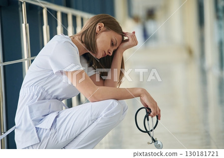 Sitting, taking a break, tired. Female doctor in white coat is in the hall Sitting, taking a break, tired. Female doctor in white coat is in the hall 130181721