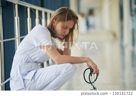 Sitting, taking a break, tired. Female doctor in white coat is in the hall Sitting, taking a break, tired. Female doctor in white coat is in the hall 130181722