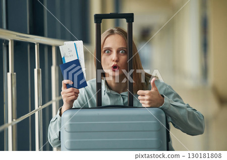 Thumb up, holding tickets. Young woman in airport hall 130181808